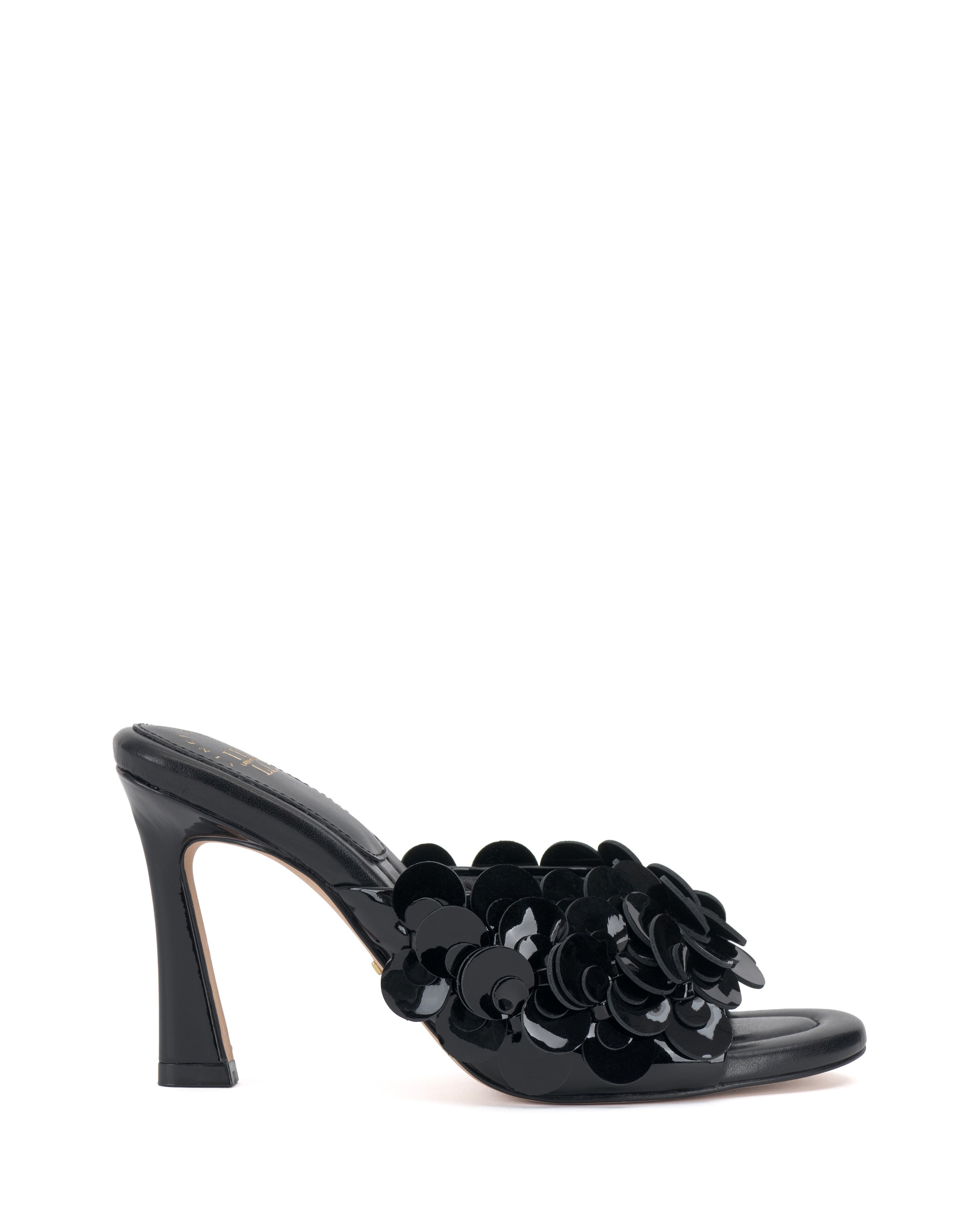 The Vince Camuto Rose Mule is a black high-heeled sandal with an open toe, glossy floral appliqués on the front strap, and a padded footbed, shown against a white background.