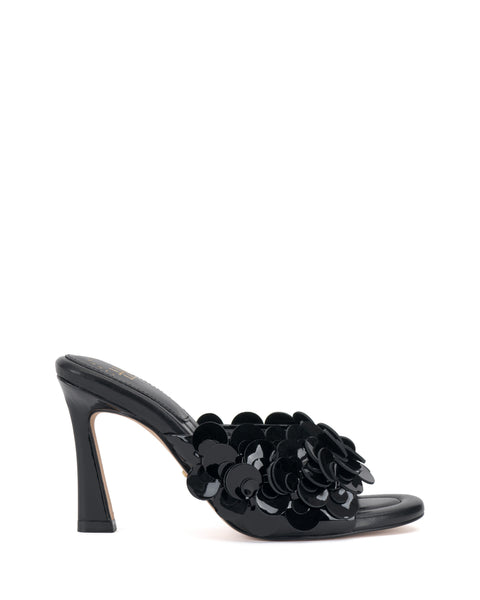 The Vince Camuto Rose Mule is a black open-toe heel with shiny black floral appliqués clustered on the upper strap and a padded footbed for comfort, shown against a white background.