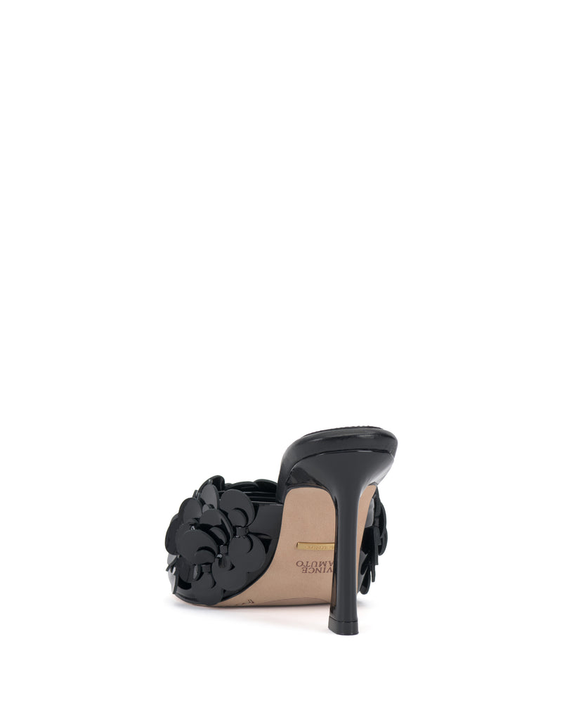The Vince Camuto Rose Mule, a black sandal with 3D floral appliqués and a padded footbed, is seen from the back on a white background, showcasing its inner sole and heel.
