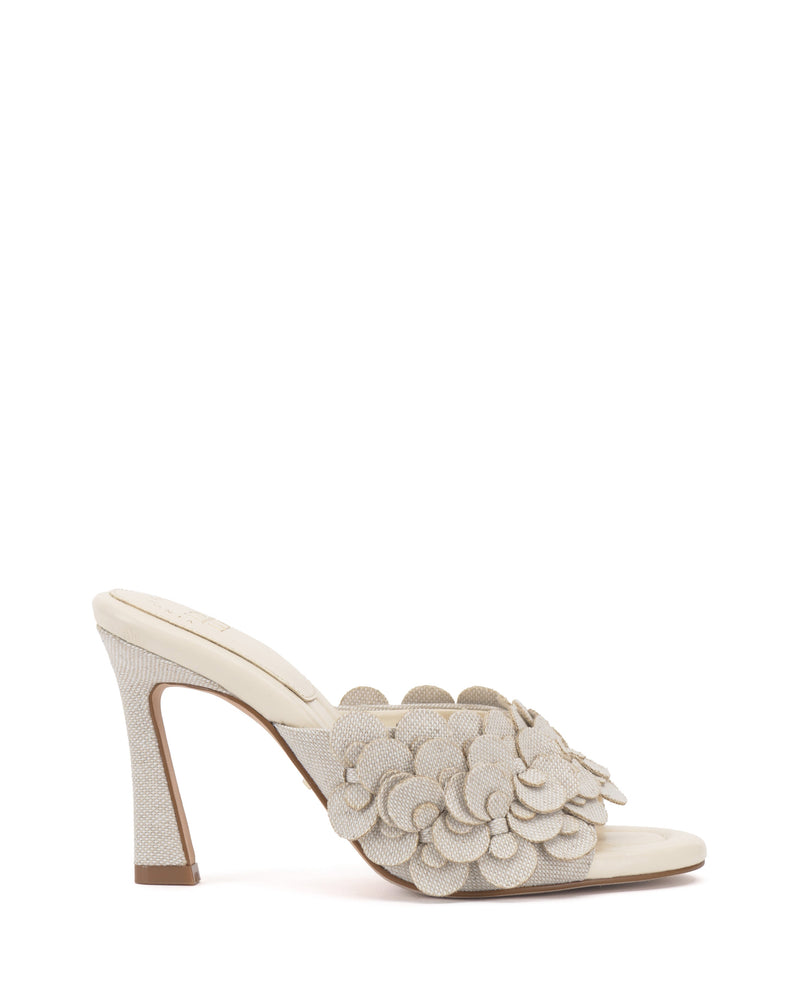 The Vince Camuto Rose Mule is a light beige high-heeled, open-toe shoe with textured fabric, layered 3D floral appliqués, a padded footbed, and matching fabric covering the sole and heel for comfort and style.