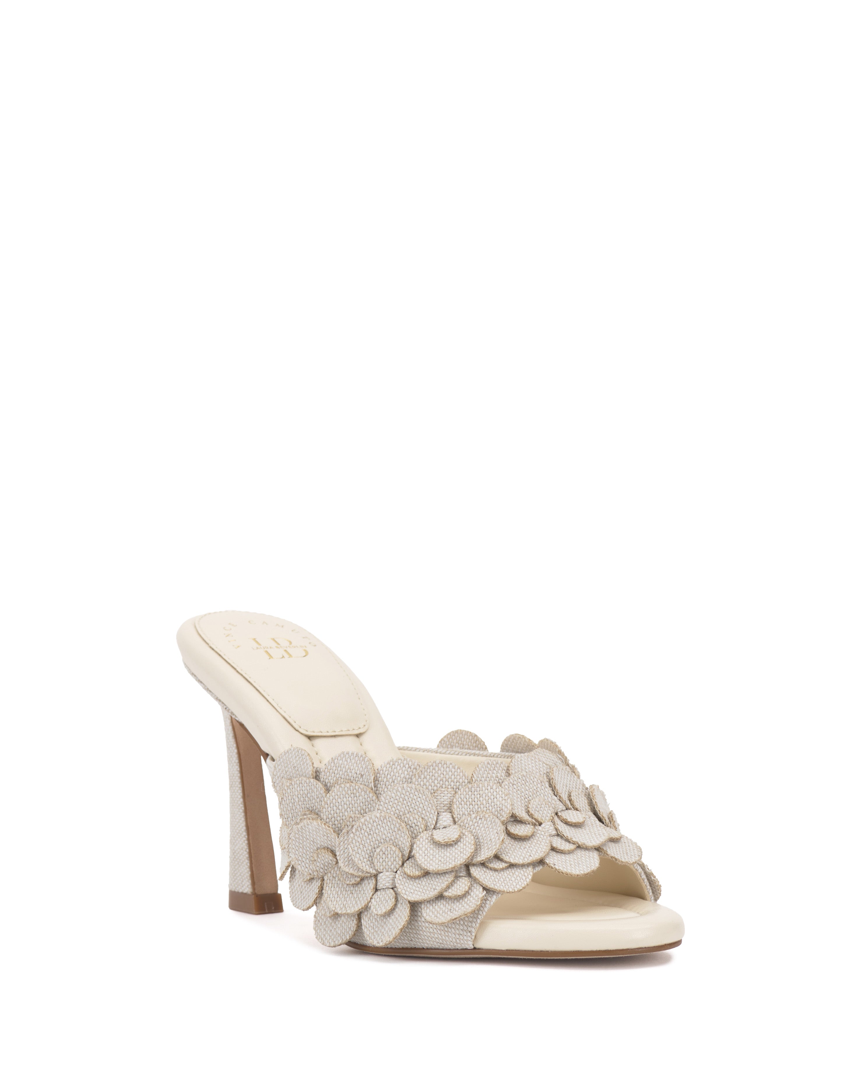 The Vince Camuto Rose Mule is a cream-colored open-toe shoe with layered fabric petal accents on the front strap and a padded footbed, shown against a white background.