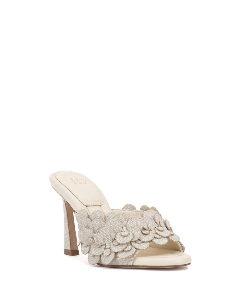The Vince Camuto Rose Mule is a cream-colored open-toe shoe with layered fabric petal accents on the front strap and a padded footbed, shown against a white background.