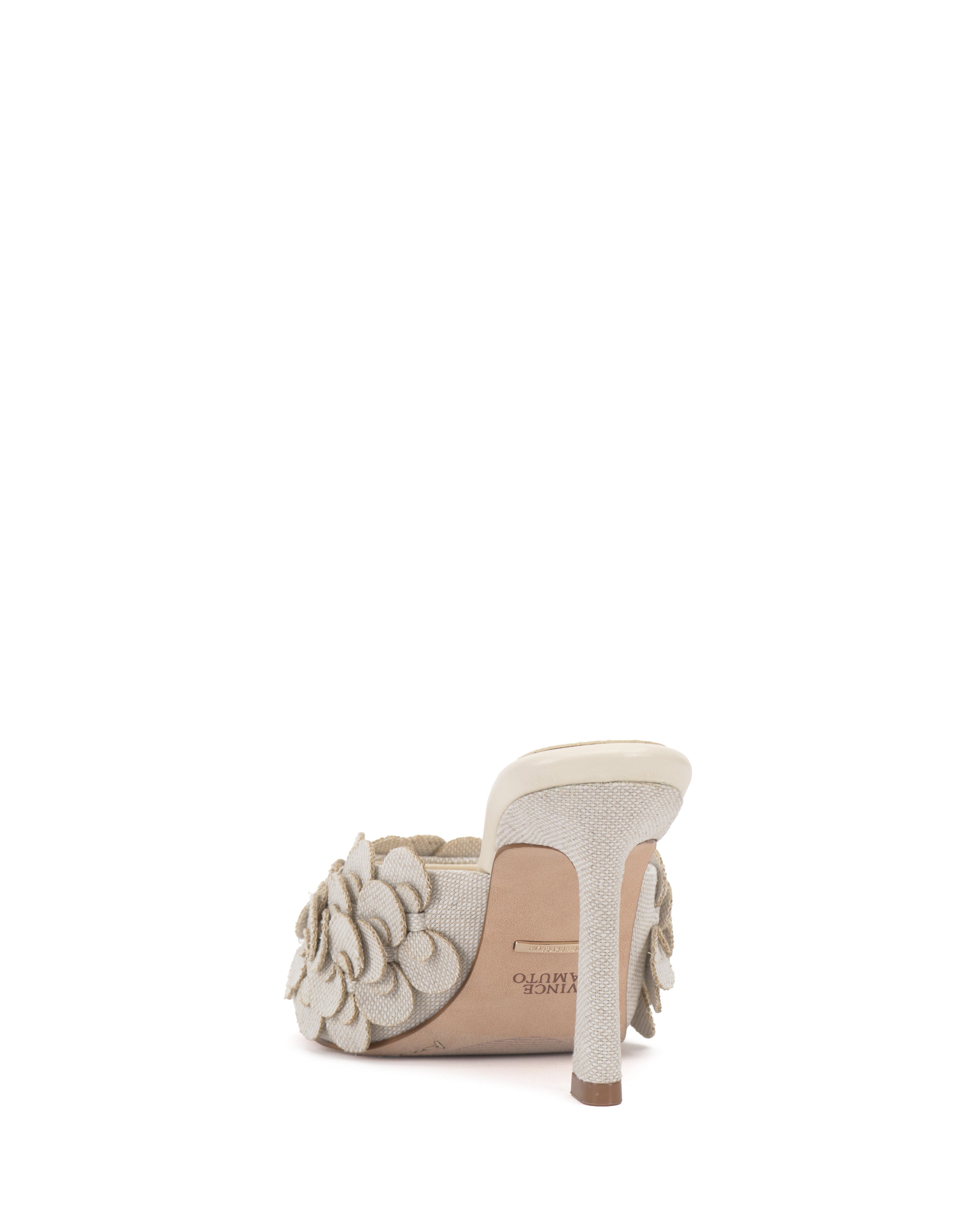 The Rose Mule by Vince Camuto is a beige 3D blossom mule with an open toe, textured fabric, floral appliqué on the strap, and a light sole, shown from the back.