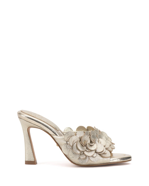 The Vince Camuto Rose Mule is a metallic gold 3D blossom mule with an open toe, layered flower appliqués on the upper strap, and a padded footbed for comfort, shown on a plain white background.