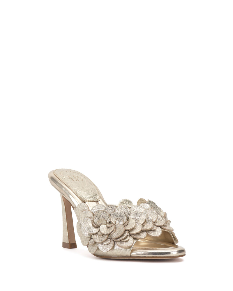 The Vince Camuto Rose Mule is a metallic gold open-toe shoe featuring 3D layered floral appliqués on the front strap and a padded footbed for comfort.