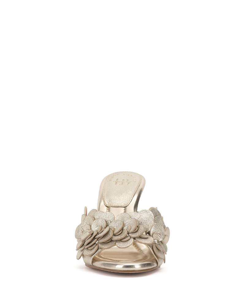 Front view of the Vince Camuto Rose Mule, a metallic gold open-toe sandal with layered flower appliqués on the strap and a padded footbed, shown against a white background.