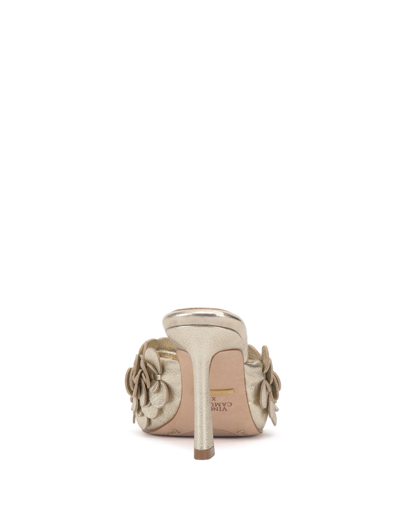 A rear view of the Vince Camuto Rose Mule in gold, featuring 3D floral details on both sides and a padded footbed, displayed against a white background.