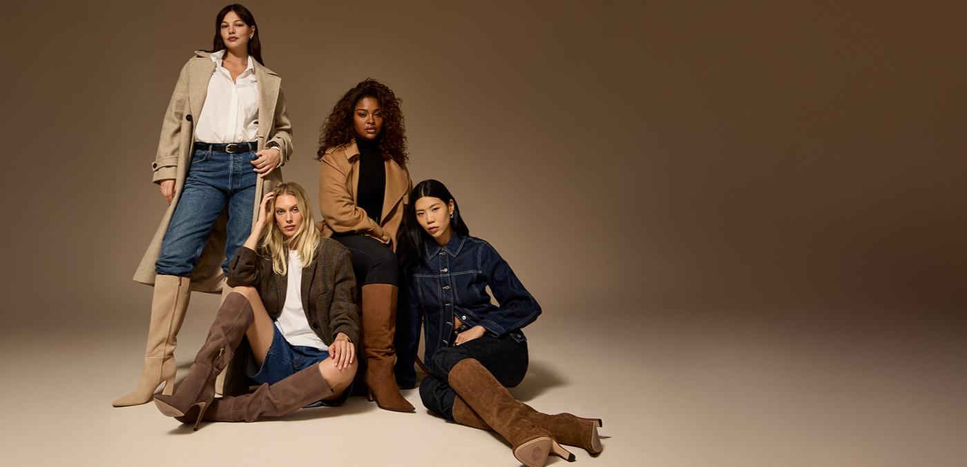 Four women posing together in a studio setting with a neutral background