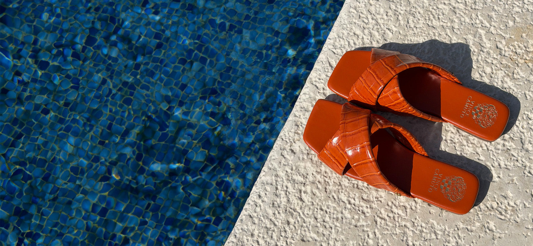 Pair of orange sandals on a poolside ledge with blue water in the background