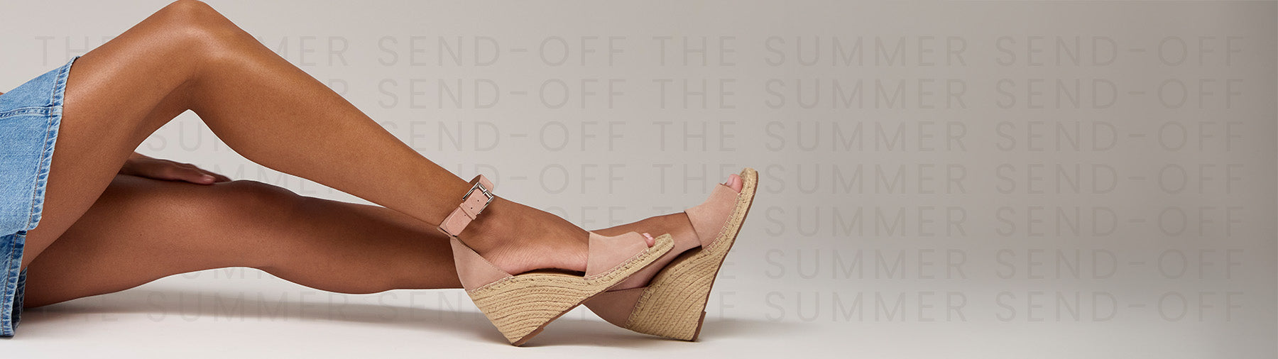 A close-up of a person's legs wearing light pink wedge sandals with a single-strap design and a beige woven platform wedge heel, posed against a light gray studio background with a faint repeating watermark.
