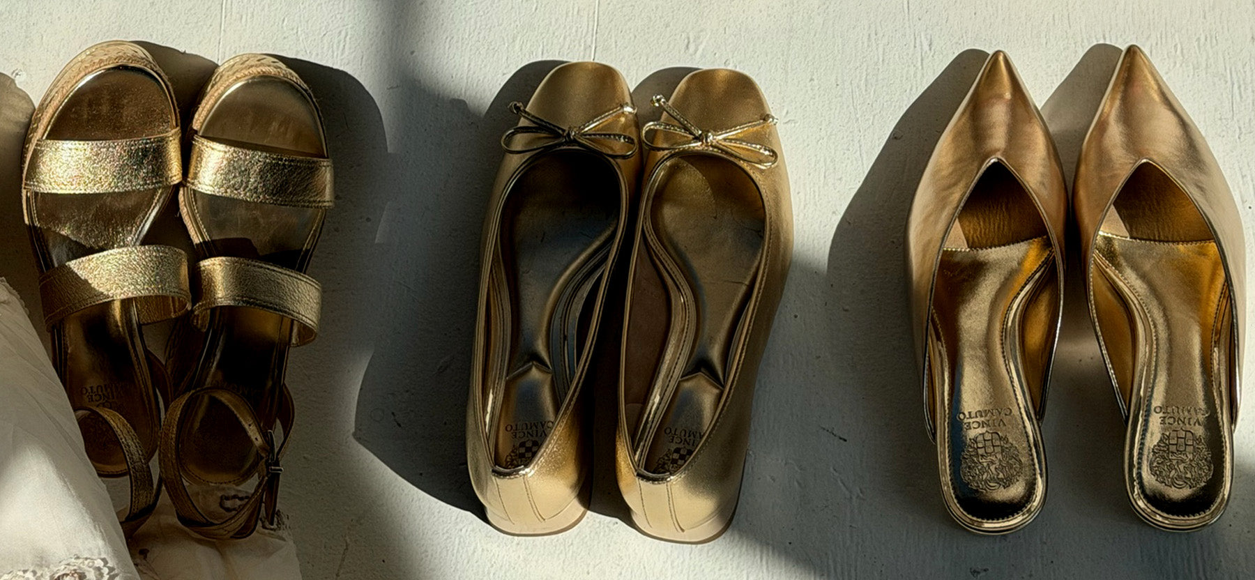 Three pairs of metallic gold women's shoes arranged side by side on a white surface under harsh direct sunlight. The left pair consists of strappy sandals, the middle pair of ballet flats with a bow detail, and the right pair of pointed-toe pumps.