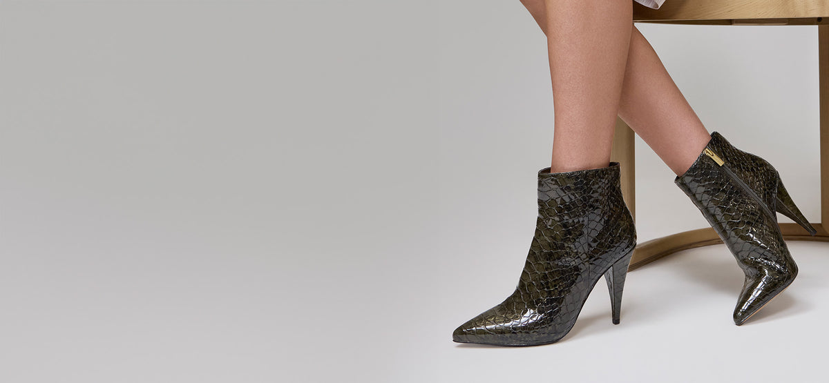 Close-up of snake skin leather booties with a gold zipper on a white studio background.