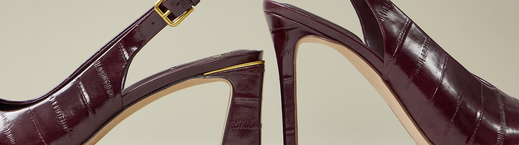 A pair of deep burgundy crocodile-embossed slingback high heels with gold buckle details, shown from side-profile views against a neutral beige background.