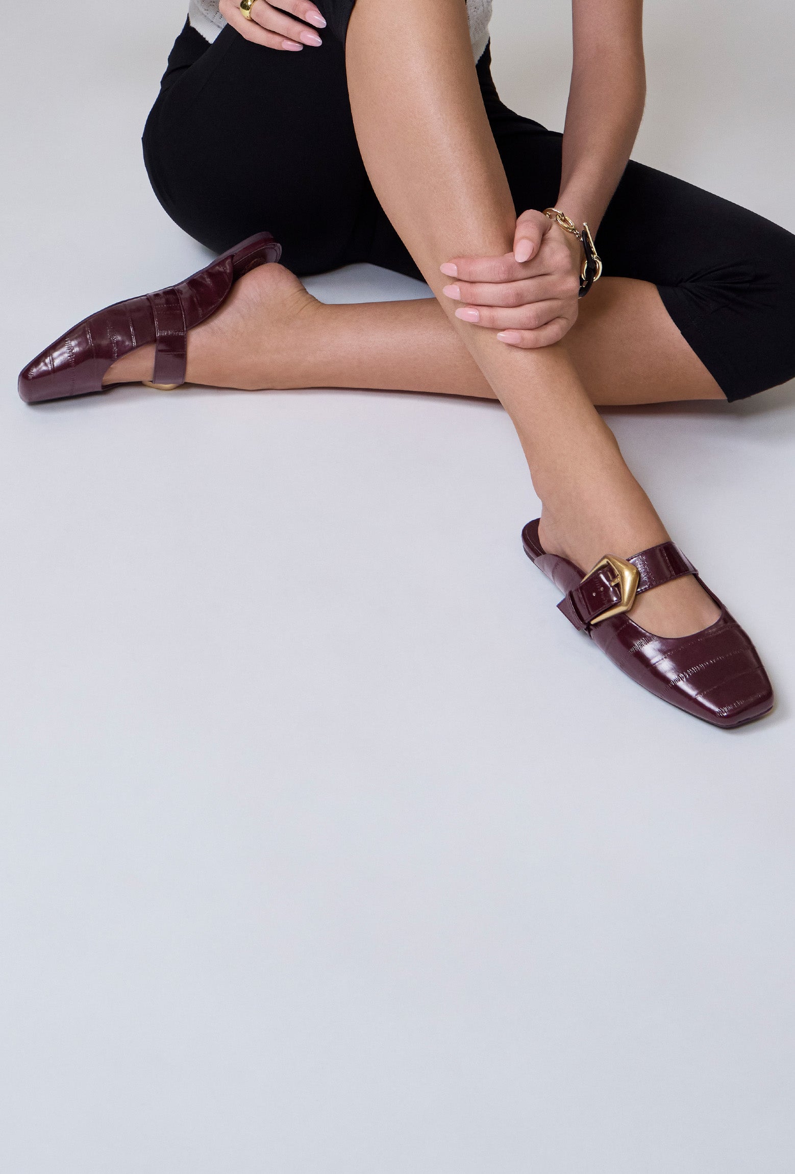 Person wearing burgundy shoes with gold buckles on a light gray background