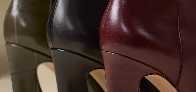 Close-up of three high-heeled boots in dark olive green, black, and burgundy leather, showing the smooth texture and heel design.