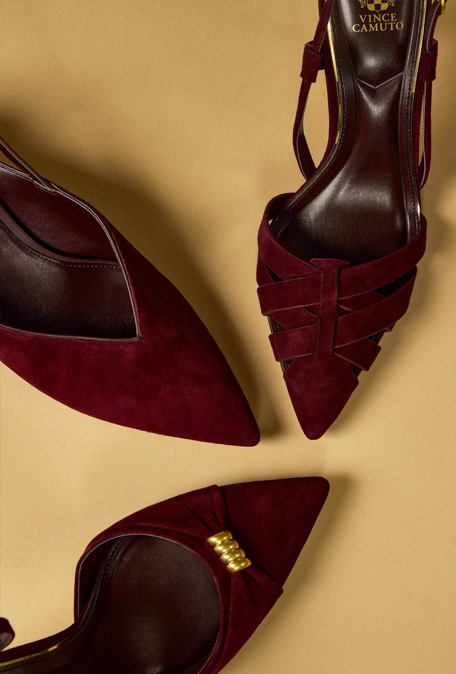 Three views of a pair of pointed-toe high heels in deep burgundy suede and leather, featuring crisscrossing straps on the toe, a slingback design, and a small gold buckle detail, displayed on a warm beige background. The brand name 'VINCE CAMUTO' is visible on the insole.