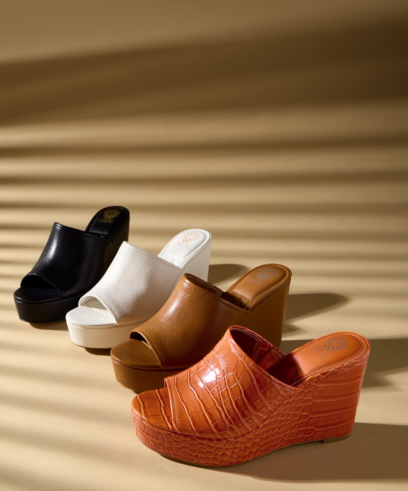 Four pairs of wedge sandals in black, white, brown, and orange on a beige background.