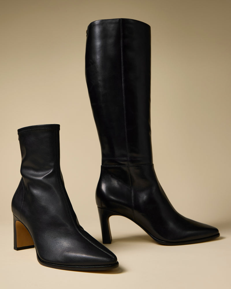 The Vince Camuto Jorela Narrow Calf Knee High Boot in black is displayed alongside a matching ankle-length heeled boot, both featuring smooth leather construction and pointed toes against a beige background.