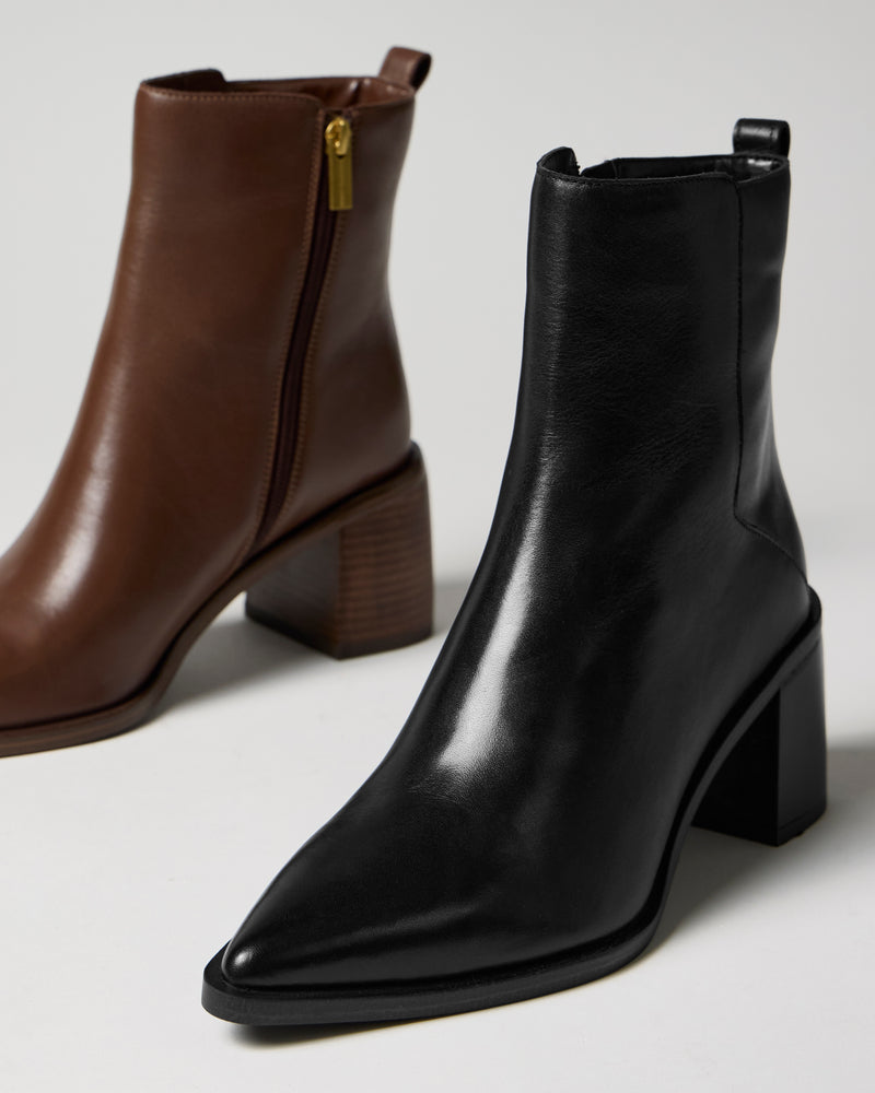 Two pairs of the Lorelai Bootie by Vince Camuto are displayed on a plain, light background. Both feature pointed toes, block heels, and a modern silhouette: one is black with a side zipper, while the other is brown with a gold zipper and wood-textured heel.