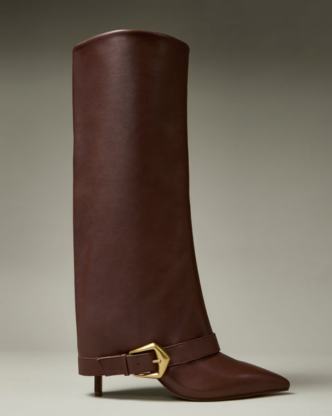 The Margee Cuff Knee High Boot by Vince Camuto is a tall, brown leather boot featuring a pointed toe, low heel, and a gold buckle strap detail at the ankle, displayed against a neutral background.