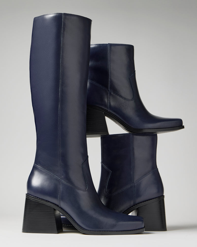 A pair of Sybren Bootie tall, navy blue leather boots by Vince Camuto, featuring a structured silhouette and chunky block heel, stacked stylishly against a neutral background.