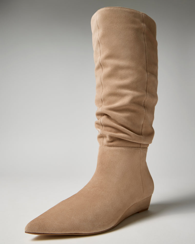 The Vanisa Knee High Boot by Vince Camuto is pictured as a single tan suede boot featuring a pointed toe and a subtle wedge heel, set against a plain light background.