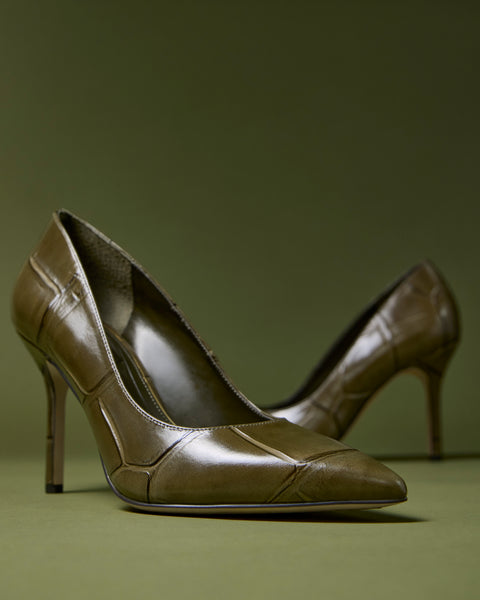 The Maisha Pump by Vince Camuto, featuring an olive green hue and pointed toes, is displayed on a matching green surface, with one shoe in sharp focus at the front and the other softly blurred in the background.