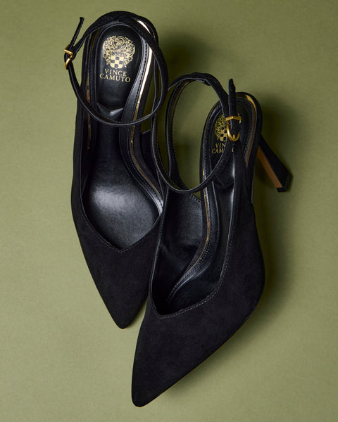 A pair of Vince Camuto Nellah Pumps featuring black, pointed toes, ankle straps with gold buckles, displayed on a green background.