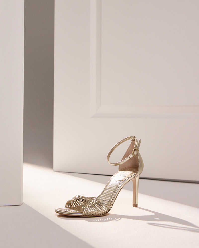 Vince Camuto Blaine Sandal in metallic gold, featuring a reptile-embossed stiletto, a skinny ankle strap, and multi-strap knotted toe detail.