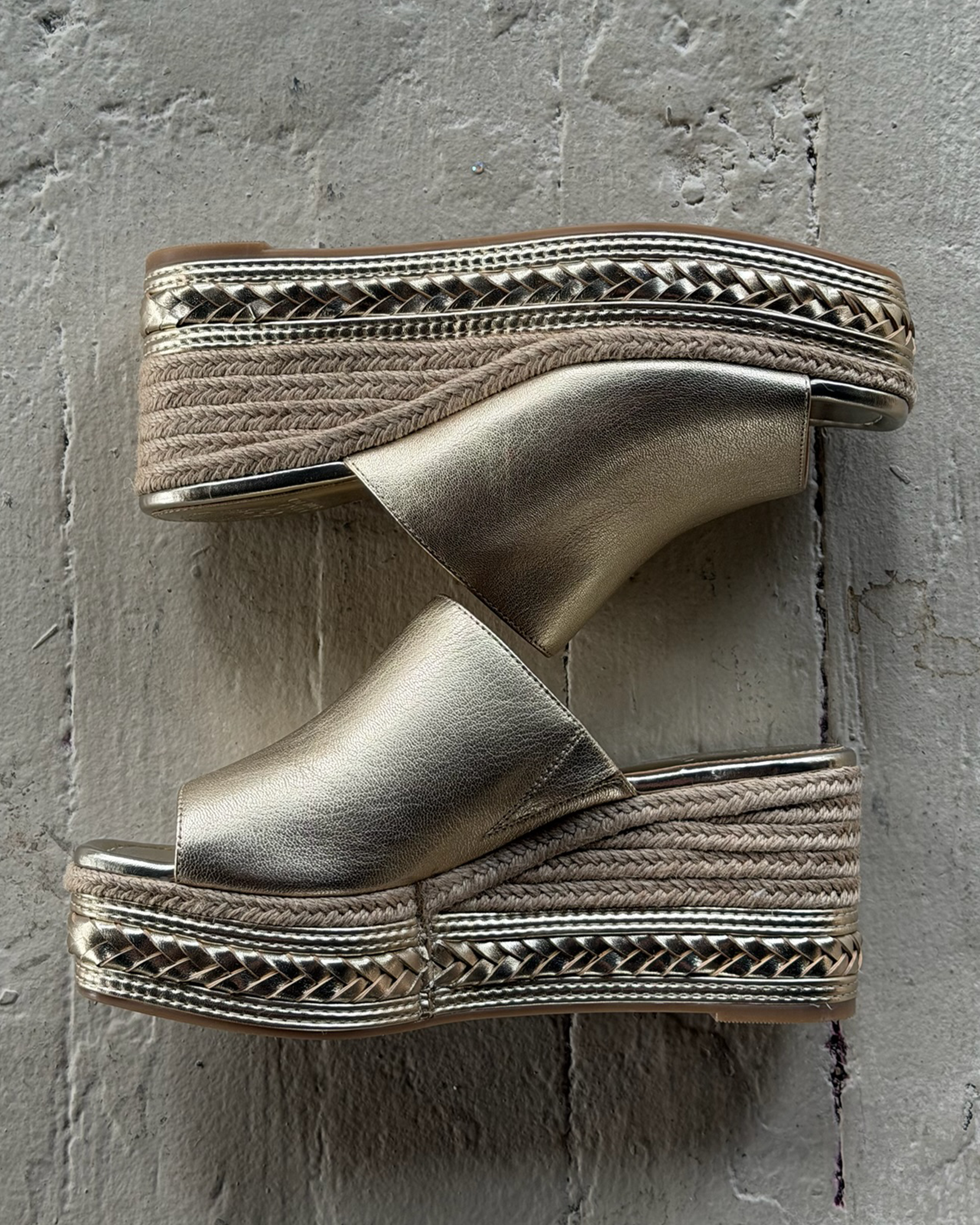 The Vince Camuto Lierna Espadrille Wedge Sandals feature gold metallic uppers, woven jute platform soles, and open toes, shown side by side on a textured gray surface.