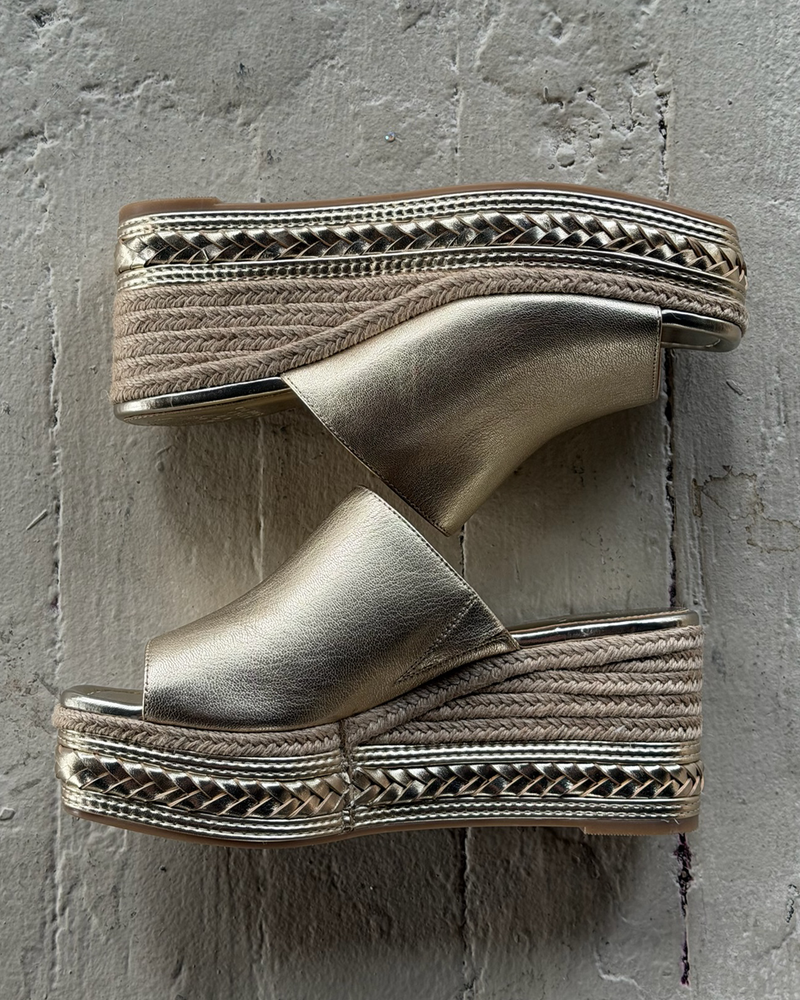 The Vince Camuto Lierna Espadrille Wedge Sandals feature gold metallic uppers, woven jute platform soles, and open toes, shown side by side on a textured gray surface.