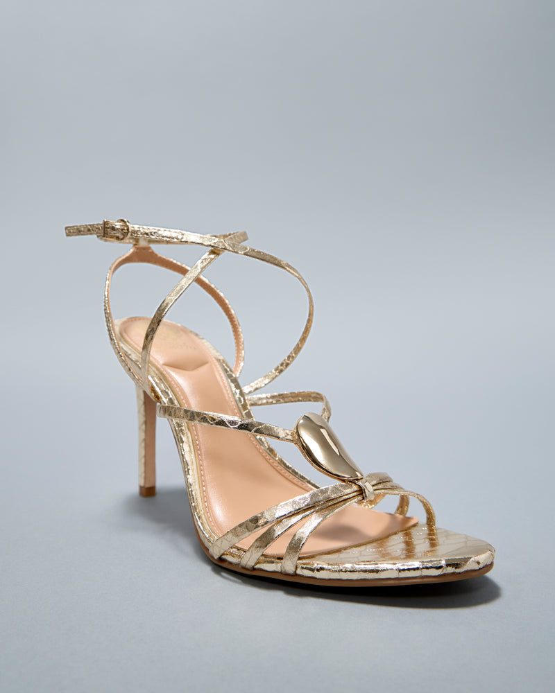 The Vince Camuto Arlein Sandal features gold straps, a sharp heel, textured finish, ankle strap, and metallic front detail—ideal for night-outs. Shown against a plain light gray background.