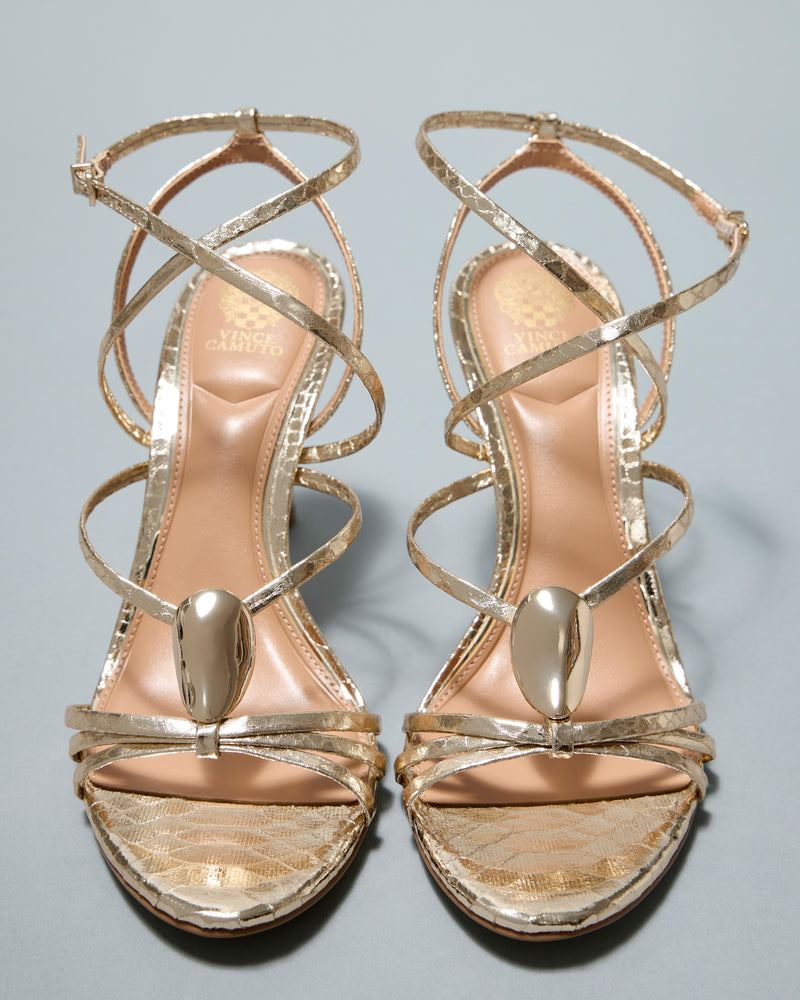 Step out in style with the Vince Camuto Arlein Sandal, featuring a sharp heel, metallic gold crisscross straps, and oval gold accents—an elegant choice to elevate your night-out look. Displayed on a neutral background.