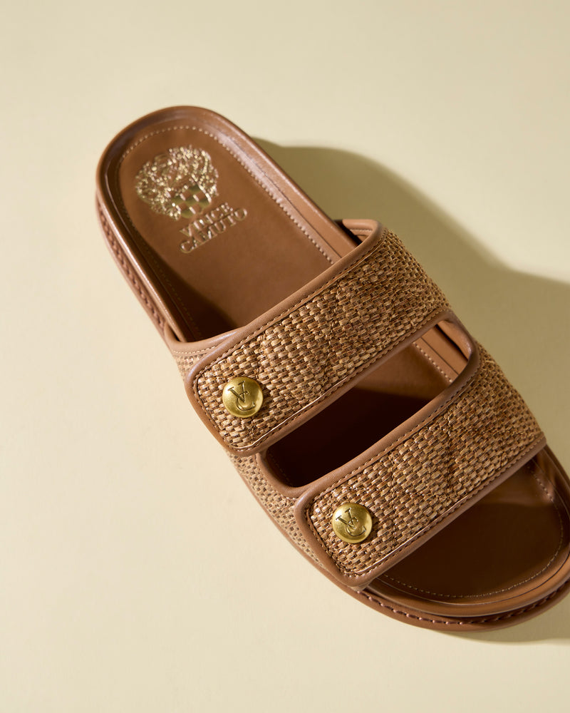 The Graysin Slide by Vince Camuto is a brown sandal with quilted double straps, gold-toned button accents, and the Vince Camuto logo on the insole, shown on a light beige background.