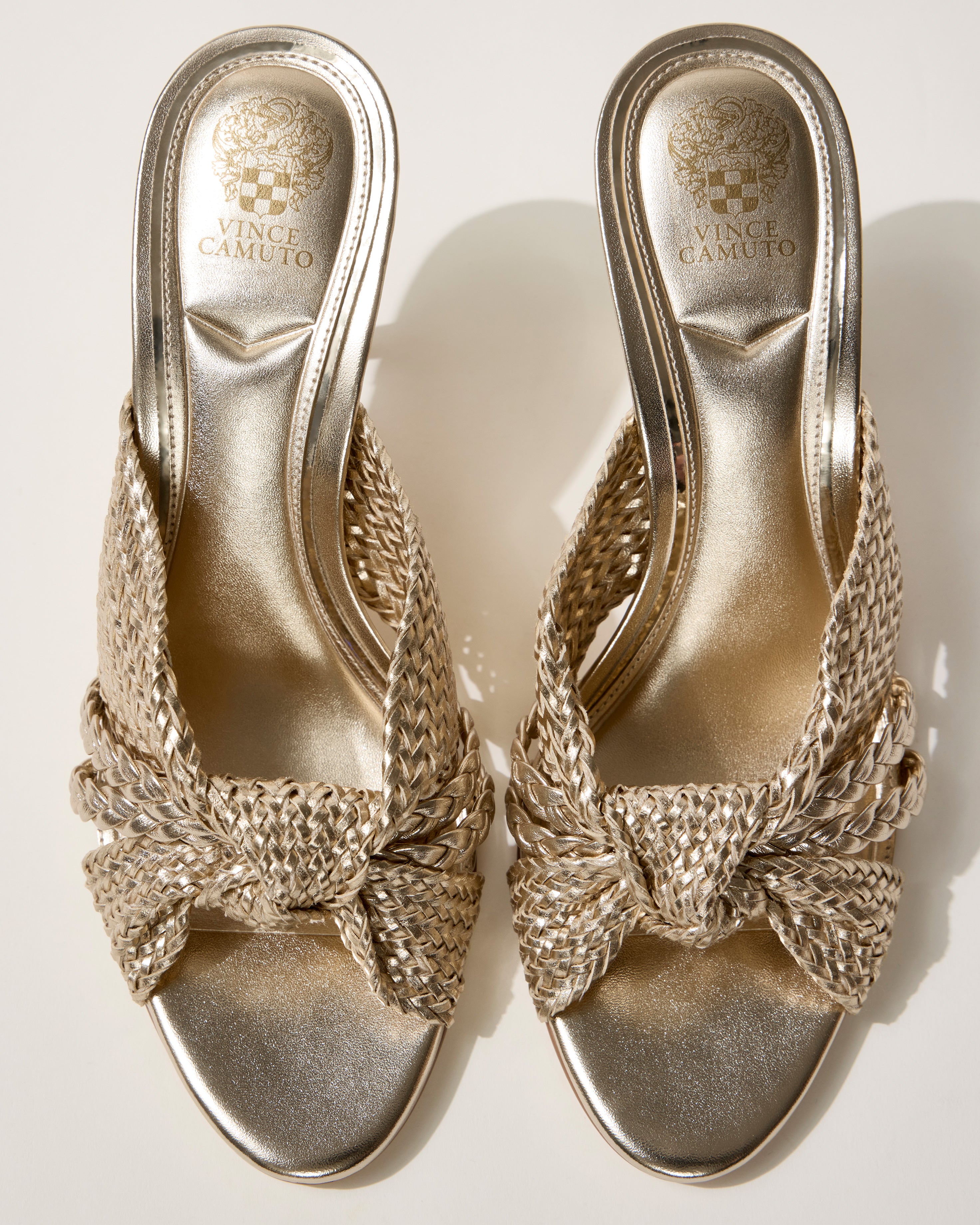A pair of Vince Camuto Pheya Mule high-heeled sandals in metallic gold with a woven design and textured open-toe straps are displayed side by side on a light background.
