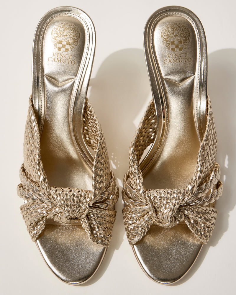 A pair of Vince Camuto Pheya Mule high-heeled sandals in metallic gold with a woven design and textured open-toe straps are displayed side by side on a light background.