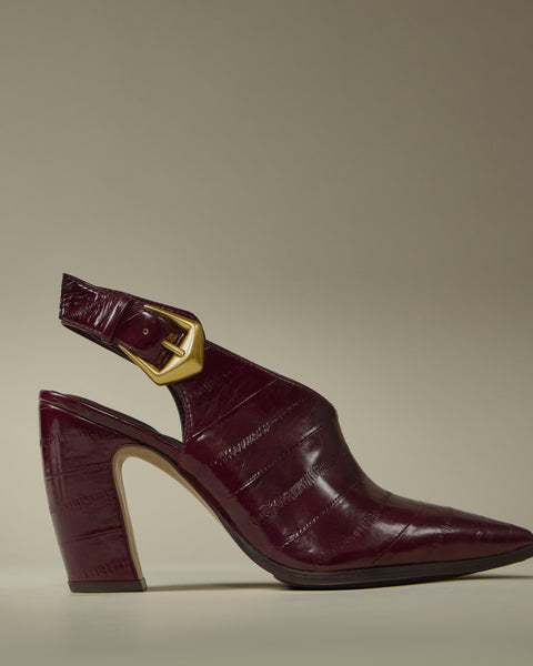 The Vince Camuto Baylez Buckled Mule features a maroon, crocodile-textured slingback design with a pointed toe, block heel, and gold buckle strap, shown against a plain beige background.