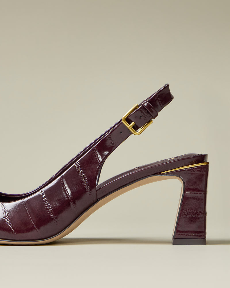 A close-up side view of the Vince Camuto Hamden Buckle Slingback in dark burgundy crocodile texture with a mid-height block heel and gold buckle strap, shown against a neutral beige background.
