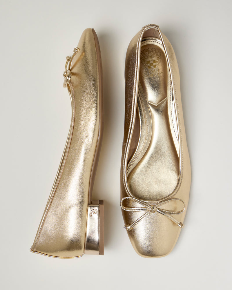The Vince Camuto Jenlea Ballet Flat features metallic gold color, small bows on the square toes, and low block heels, shown from side and top views on a light background.