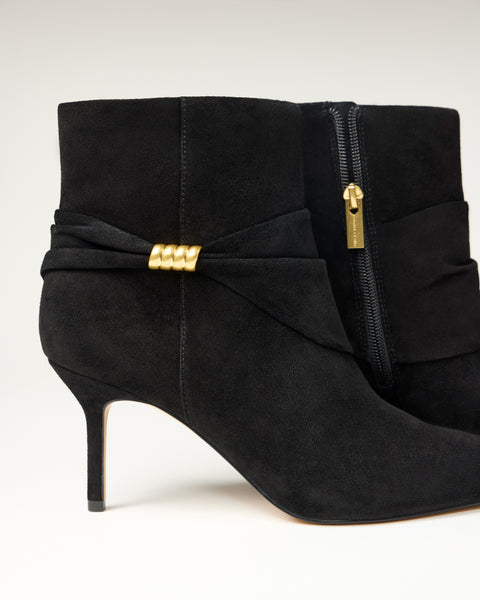 The Vince Camuto Murlea Bootie features black suede, pointed toes, stiletto heels, a gold accent on the side, and a visible zipper with a gold pull tab, set against a plain background.