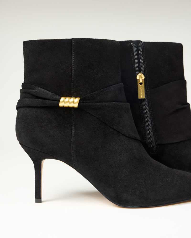 The Vince Camuto Murlea Bootie features black suede, pointed toes, stiletto heels, a gold accent on the side, and a visible zipper with a gold pull tab, set against a plain background.