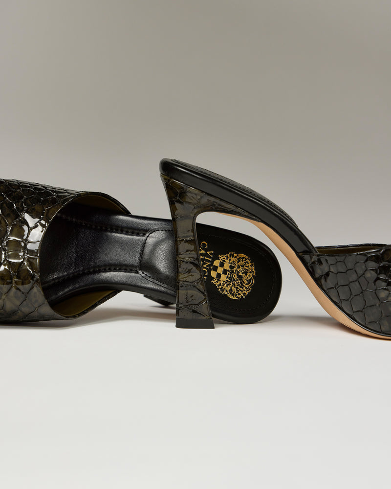 The Vince Camuto Paigely Mule in black features a crocodile-textured design with chic flared high heels and a gold logo on the insole, displayed on a neutral background—one upright and one lying on its side.