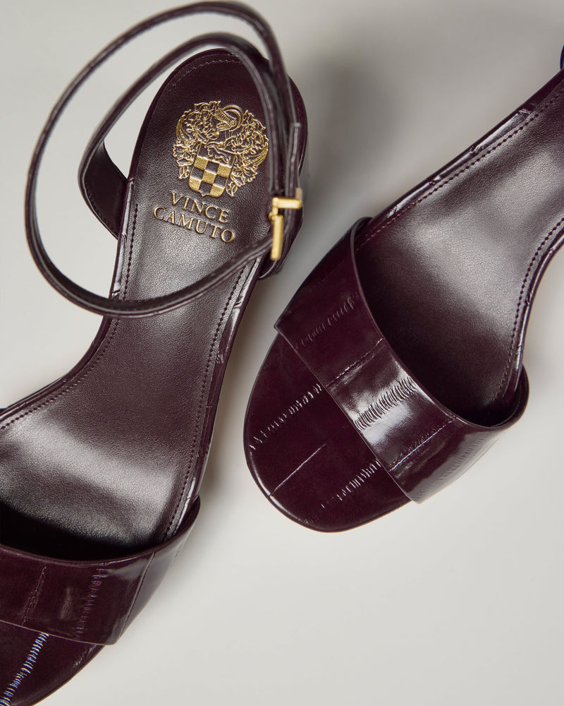 Two Vince Camuto Pendreya Platform Sandals in dark burgundy, featuring block heels, gold logo accents, and ankle straps, displayed on a light surface.