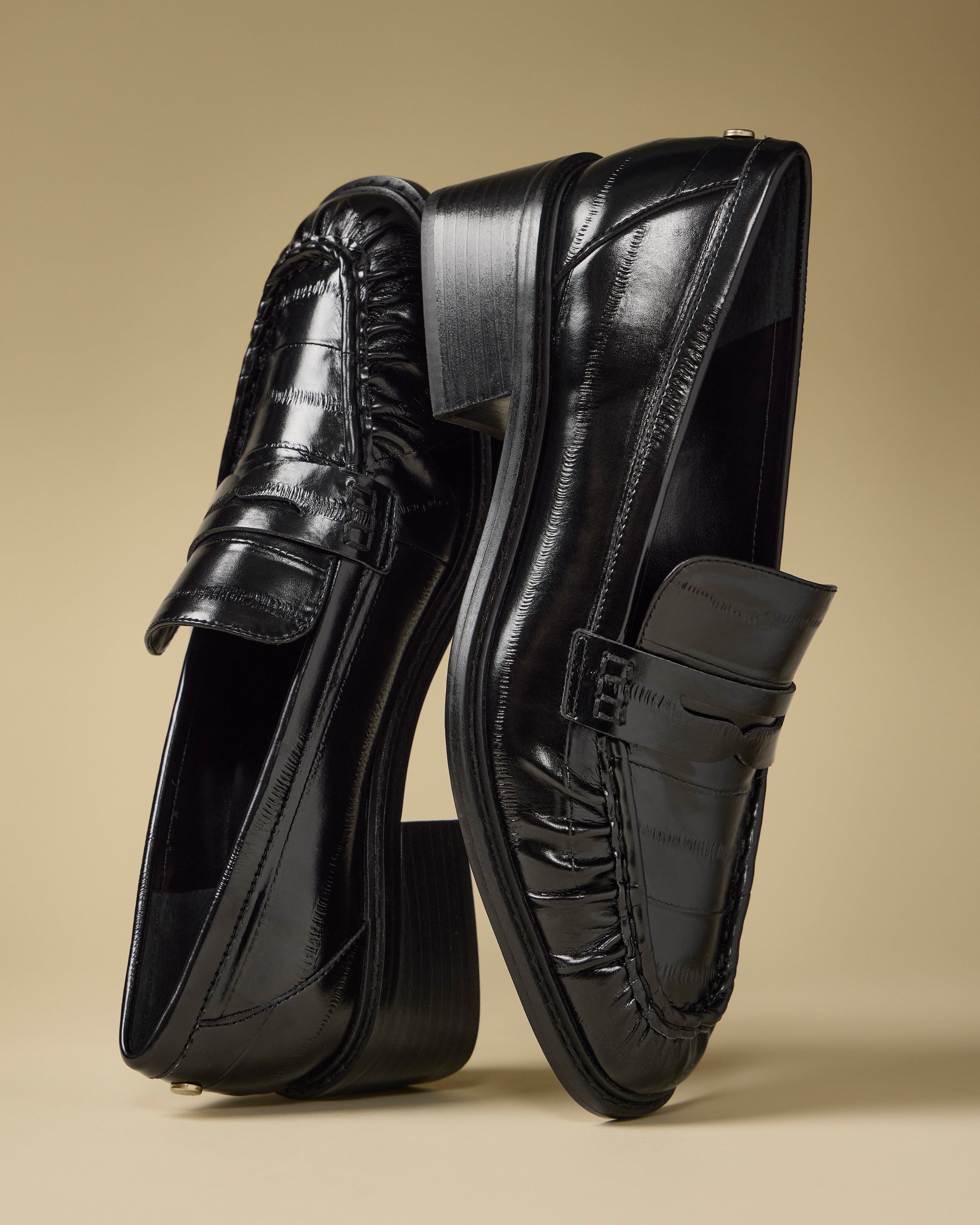 The Vince Camuto Eshnie Block Heel Loafers in shiny black are shown on a beige background—one upright, one angled—to showcase their polished finish, detailed stitching, and subtle block heel.