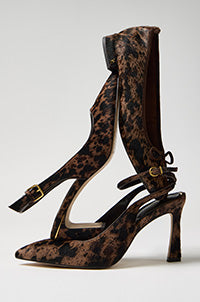 A pair of pointed-toe high heels with a brown and black leopard print pattern, featuring ankle straps with gold-tone buckles, photographed on a light gray background.
