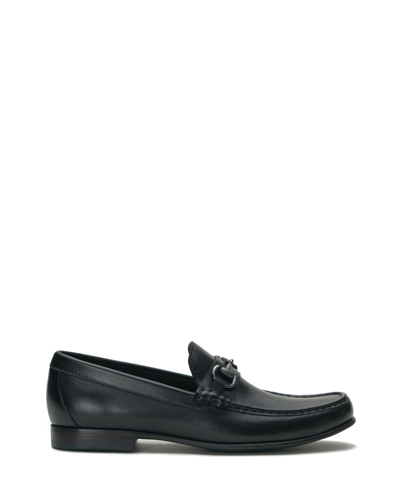 The Vince Camuto Men’s Caelan Loafer is a black leather slip-on with a low heel and buckle detail, displayed in side profile against a white background—these classic loafers are an ideal choice for stylish office footwear.