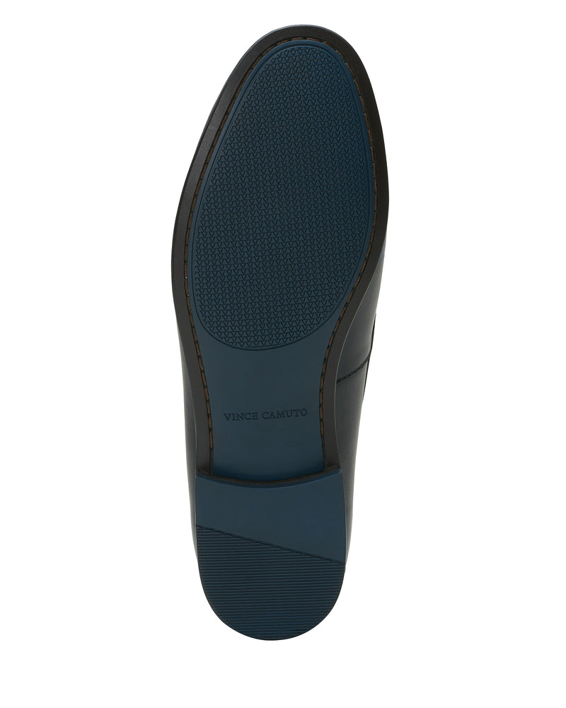 The sole of the Vince Camuto Men’s Caelan Loafer features dark leather with a blue rubber tread, moccasin toe detailing, and “Vince Camuto” embossed in the center.