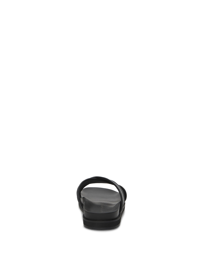 The Vince Camuto Men's Dabor Cross-Band Sandal is shown from the back, in black, with a flat sole and a single braided strap over the foot, set against a white background.