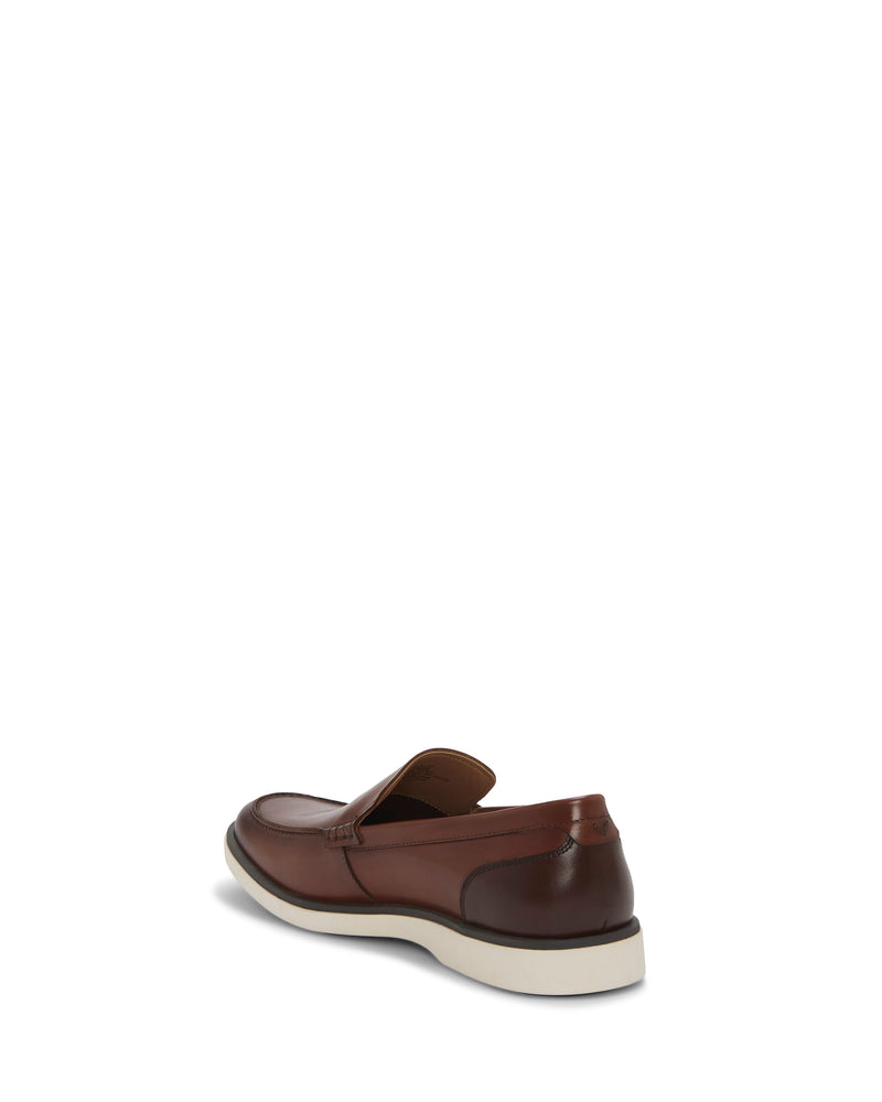 The Vince Camuto Men's Sevrin Casual Loafer, shown in brown with a white sole and EVA insole cushioning, is displayed from the back-left angle on a plain white background.