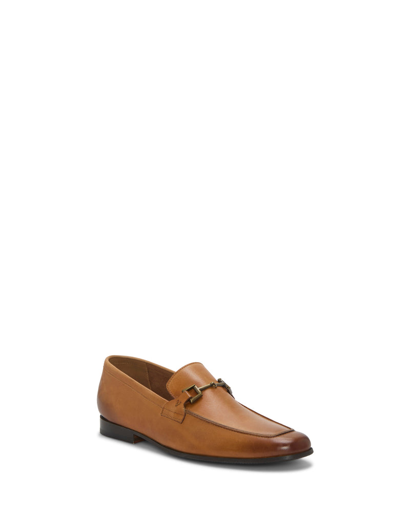 The Vince Camuto Men's Sevvano Dress Loafer is a tan leather slip-on with a sleek, rounded toe and horse bit detail, set on a low heel. Shown on a white background.